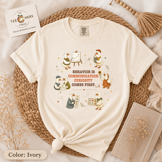 Ivory Comfort Colors t-shirt folded flat lay with illustrated duck and teacher design reading Behavior Is Communication, Curiosity Comes First - Behavior Is Communication Shirt by The Teechers Thread